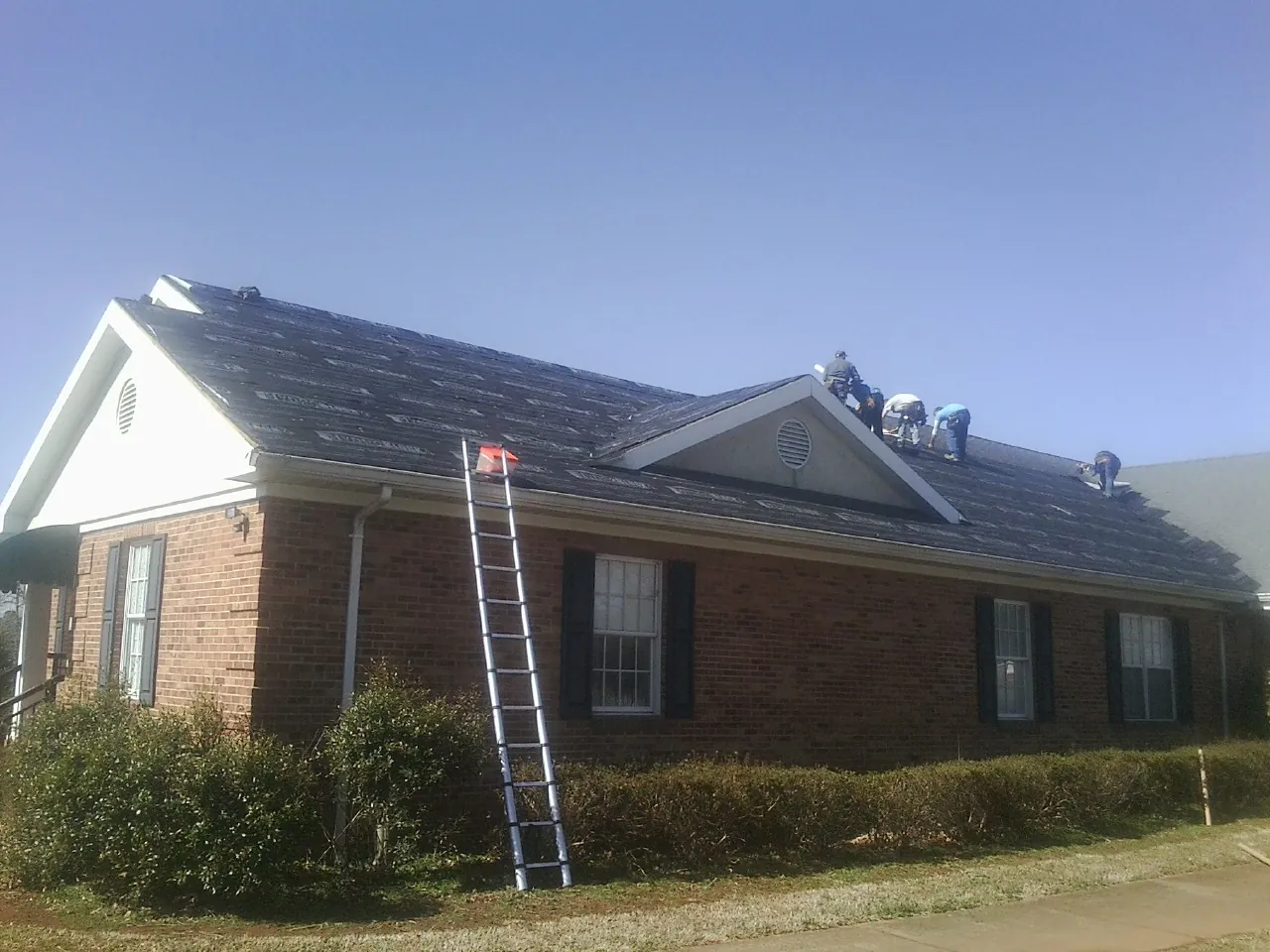 Crew tearing shingles off a brick ranch roof with a ladder set — Emergency Roof Repair work by our crew in Eagleville