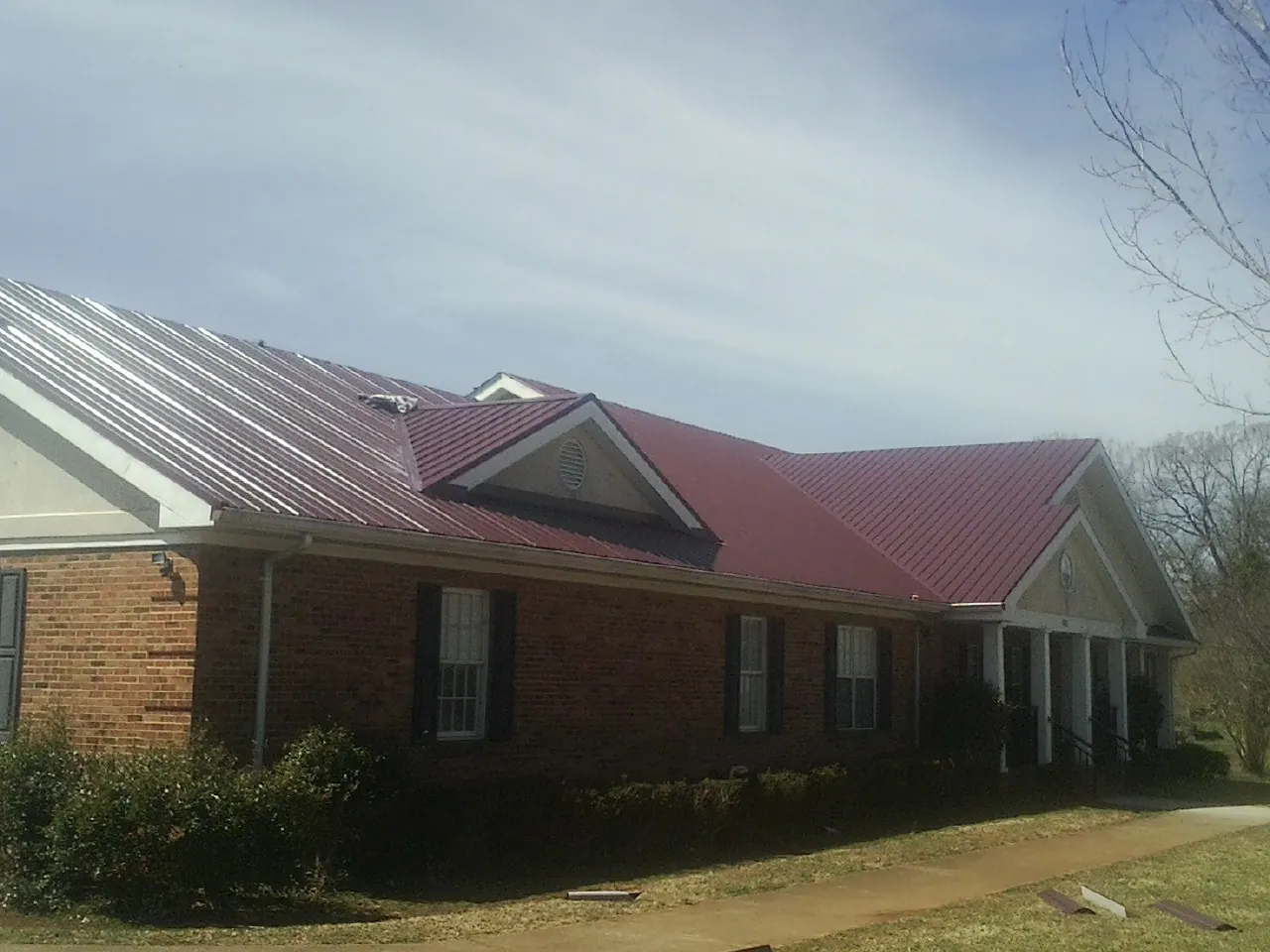 Red metal roof with gabled entries on a long brick building, from a Hail Damage Roof Repair job in Eagleville