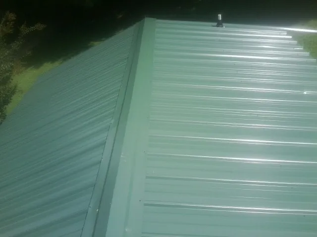 New green metal panels meeting at the ridge of a roof — Flat Roof Repair work by our crew in Eagleville