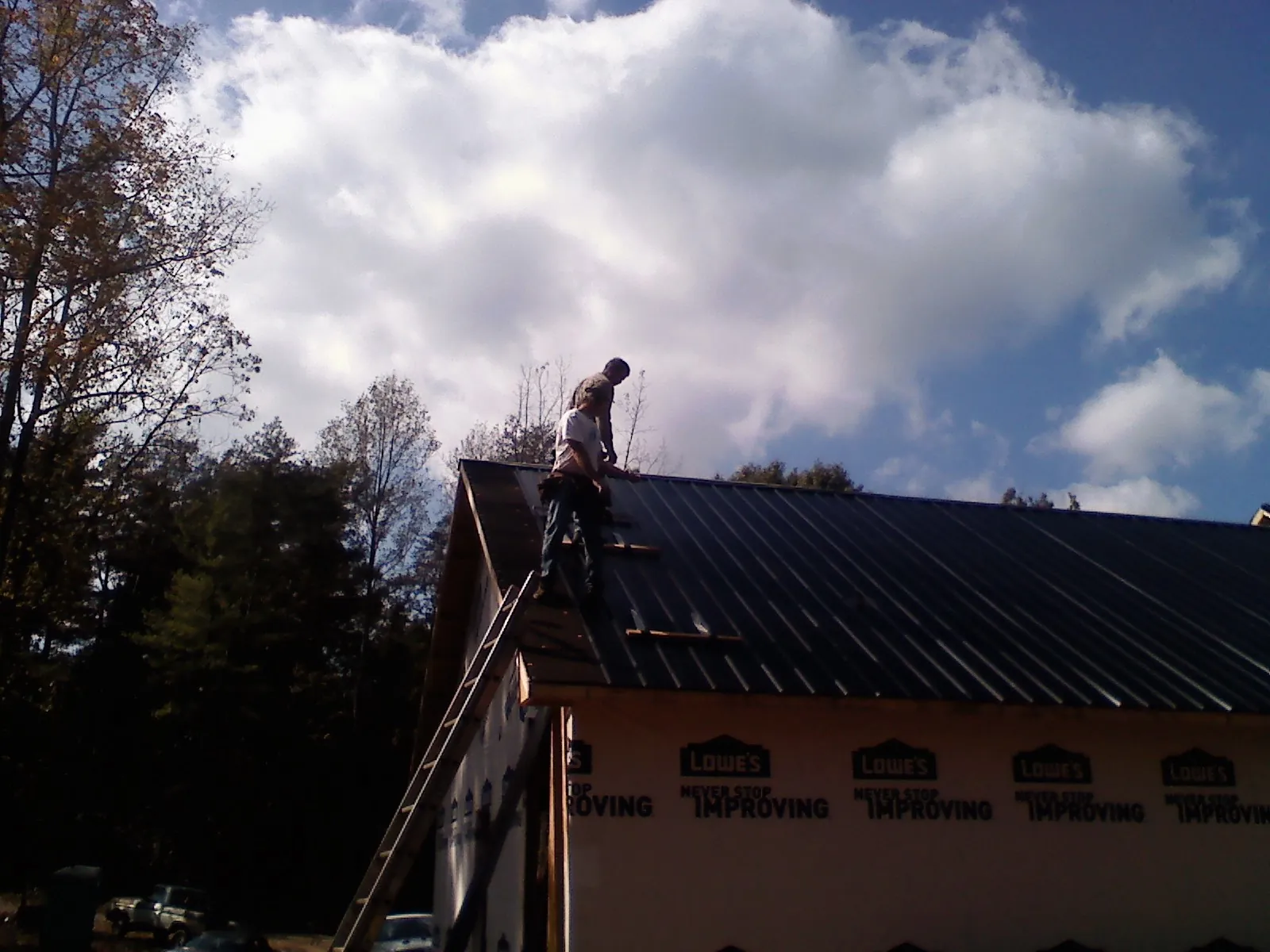 Roofer fastening dark metal panels high against a cloudy sky, from a Roof Inspection job in Eagleville