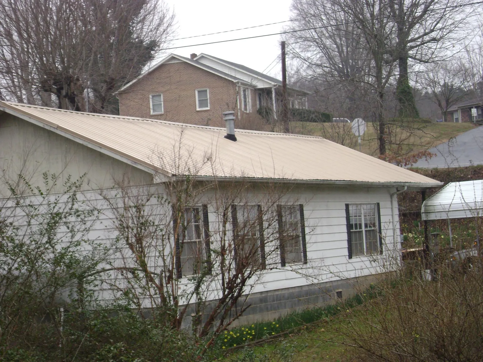 Tan metal roof on a white sided house set into a hillside — Commercial Roofing by Roofing Brothers in Eagleville