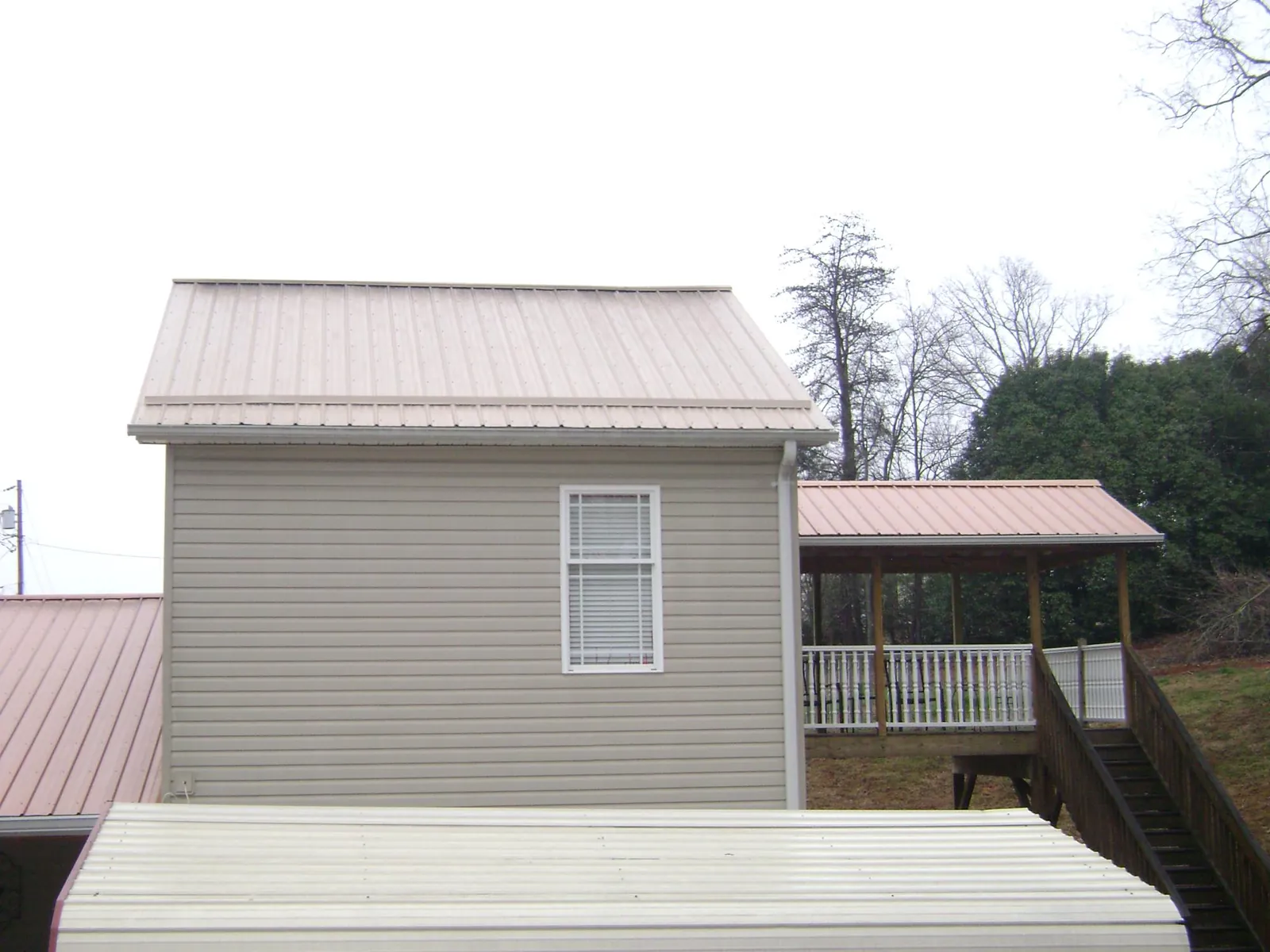 Tan metal roofs on a two story addition and attached porch, from a Roof Replacement job in Eagleville